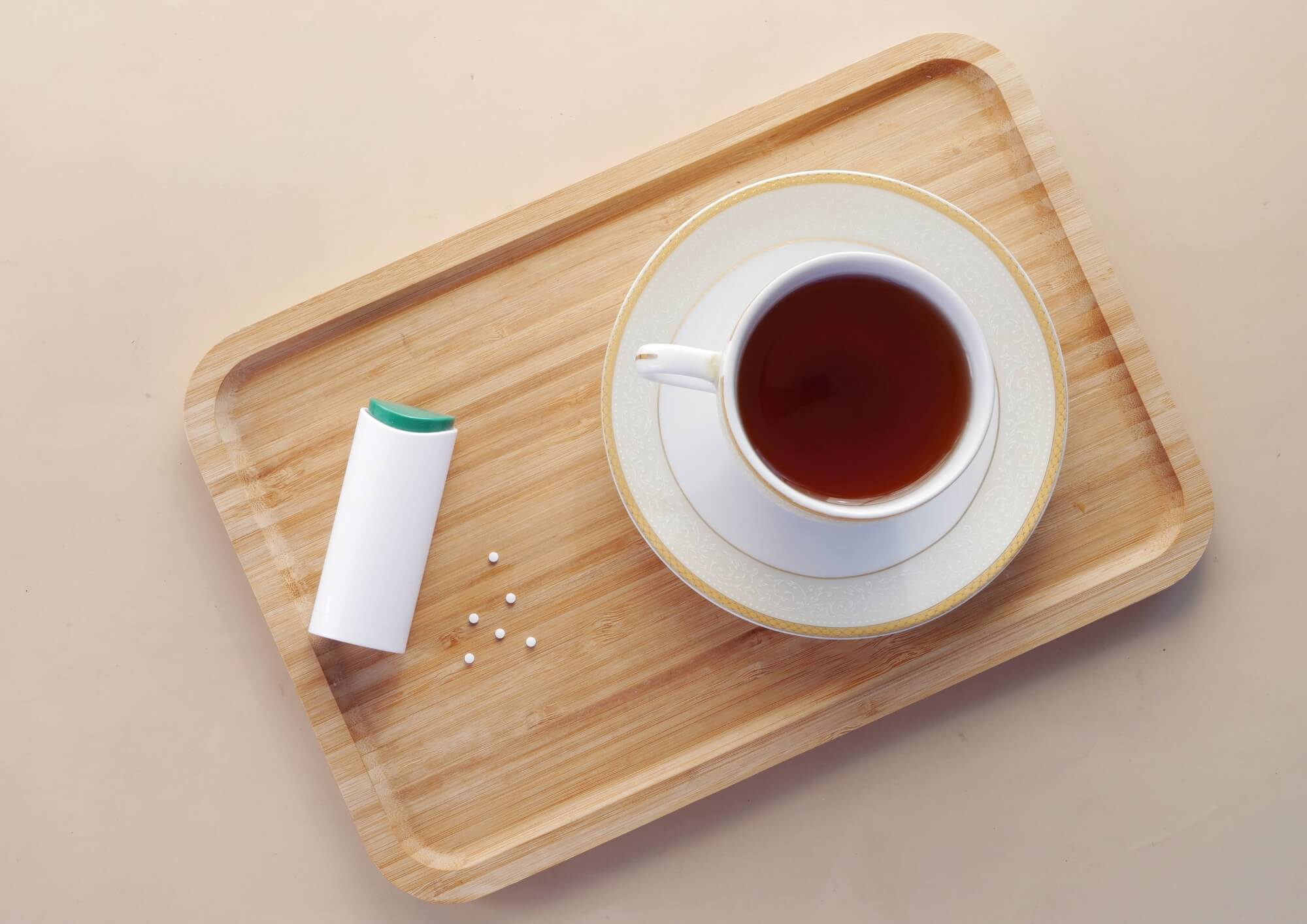 Artificial sweeteners alongside a cup of tea on a wooden tray—calorie-free sugar substitutes for a sweet taste without the extra calories