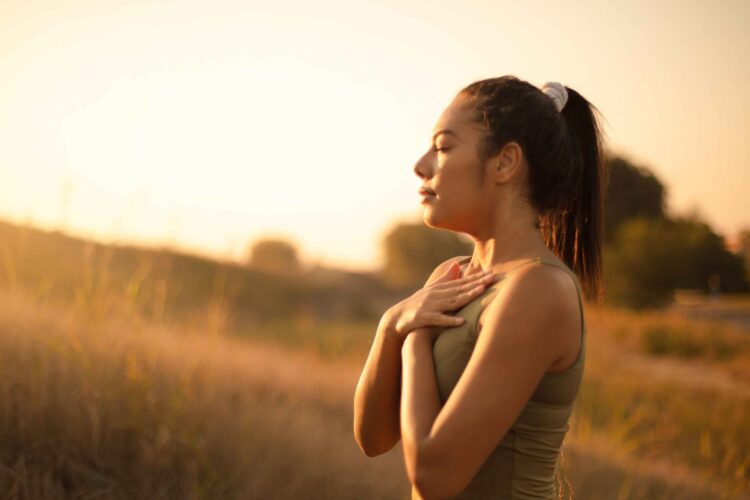 Calm woman practicing breathwork meditation at home with eyes closed and hands on her belly—illustrating natural breathwork for stress relief and relaxation.
